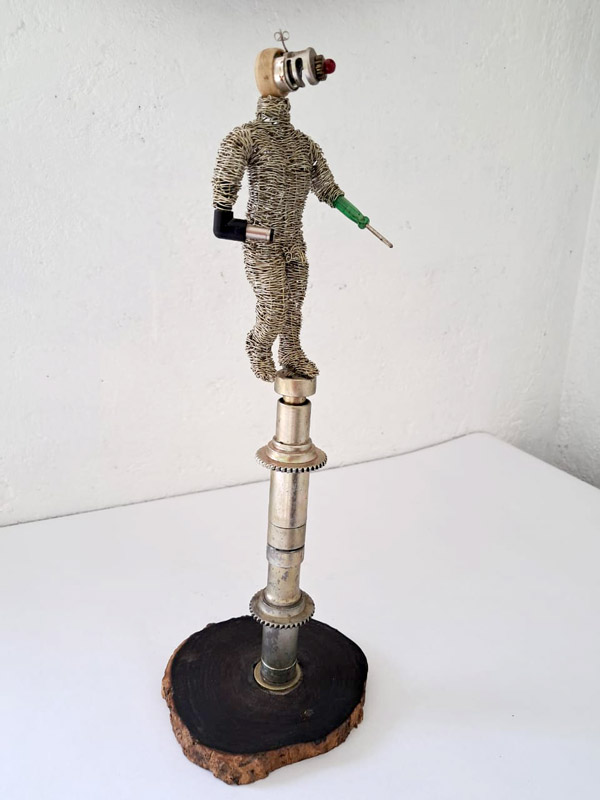 <p><em>Paso al futuro</em>. 30X12X12 cm. Madera, partes automotrices alambre de acero tejido a mano, anillo de hueso, arete de plata. 2021</p>